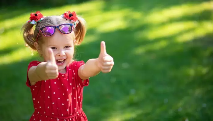 child in red dress in yard thumbs up